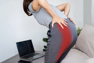 Woman experiencing sciatic nerve pain from buttock to leg due to poor posture while working at computer