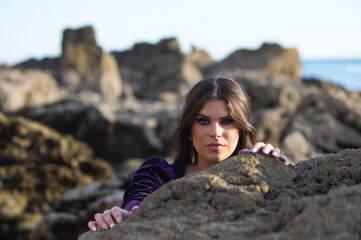 beautiful young woman dancing flamenco among the rocks by the seashore, wearing a purple velvet dress with ruffles. The gypsy woman makes different expressions with her face and hands.