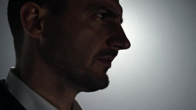 Static close-up video of a contemptuous man with a large, hooked nose expressing disdain, dramatic front lighting, solid gray background, he sneers and turns his head away in disgust