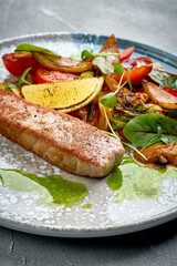 A close-up of a grilled salmon, showcasing the tender texture of the meat and the crispy exterior. The dish is served with roasted vegetables, creating a delightful contrast of textures