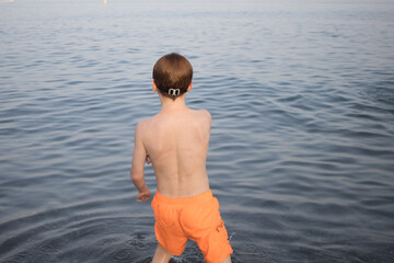 portrait of redhead boy from behind with orange swimsuit looking at the sea. Horizontal. copy space