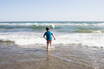 Boy redhead playing with ball on beach with blue t-sirt. Sea. Horizontal. copy space	
