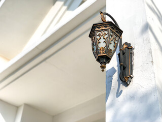 Old antique metal lamp hanging on the white wall. Vintage iron lantern at the day time, turned off. The wall lamp on the street.