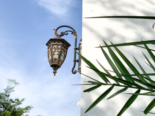 Old antique metal lamp hanging on the white wall. Vintage iron lantern at the day time, turned off. The wall lamp on the street.
