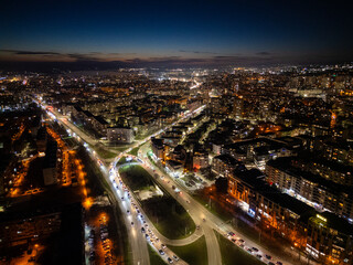 Fototapeta premium Aerial view of Varna, Bulgaria, at sunset, showcasing a vibrant cityscape with illuminated streets, moving traffic, and a glowing skyline. The coastal metropolis reflects urban energy and modern