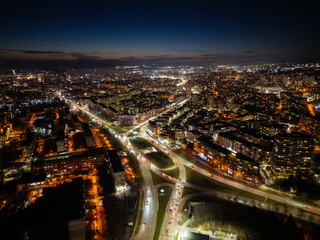 Obraz premium Aerial view of Varna, Bulgaria, at sunset, showcasing a vibrant cityscape with illuminated streets, moving traffic, and a glowing skyline. The coastal metropolis reflects urban energy and modern