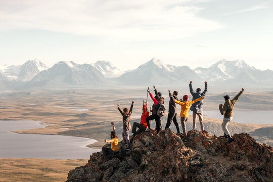 Large group of tourists diverse people hikers are standing at mountain top at winner poses with open raised arms and enjoys achievement
