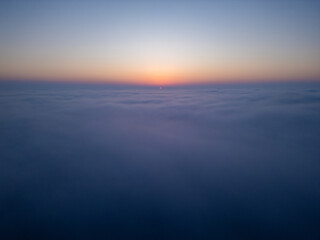 Aerial drone view above clouds at sunrise, high-altitude misty landscape with rolling fog and golden horizon, breathtaking cinematic aerial footage capturing the tranquil beauty of sky and clouds in