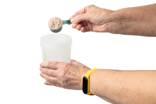 Senior female hand putting a portion of whey protein powder from a measuring spoon into a shaker, preparing a protein drink. Isolated on a transparent background