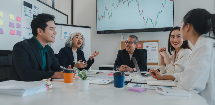 Asian businesspeople collaborating on a project in a modern office meeting room, analyzing financial charts displayed on a large screen and discussing strategies for success
