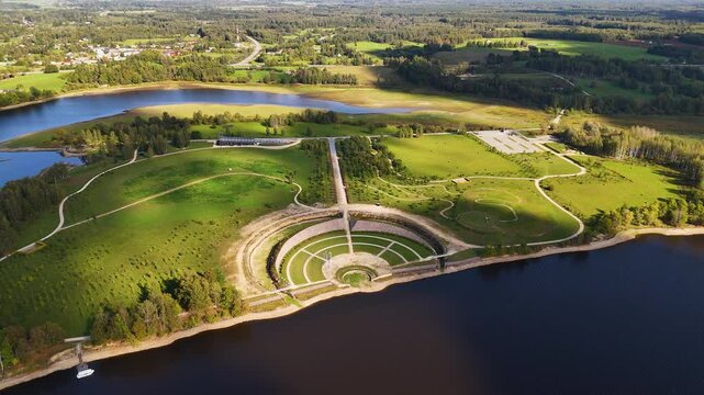 An aerial view of a stunning green park with a circular amphitheatre by the water. Kokneses pilsdrupas are ruins of a castle in Koknese, Latvia.