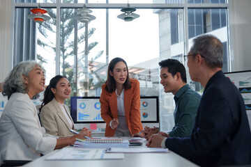 Asian business team is discussing financial charts and data displayed on computer screens during an office meeting, collaborating and analyzing business performance