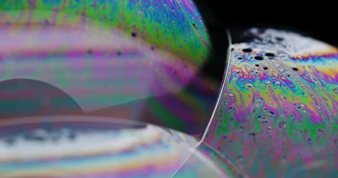 Macro shot showing colorful fluid motion on the intersection of 3 soap bubbles