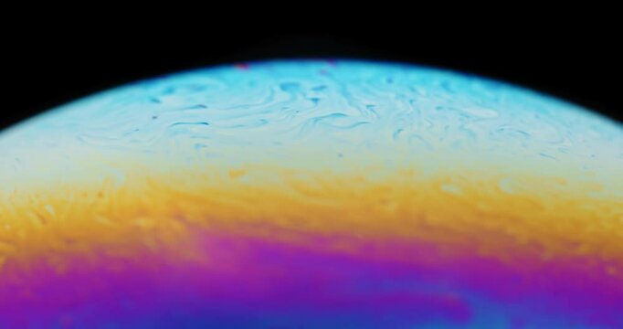 wild color patterns forming on surface of soap bubble looking like an alien planet