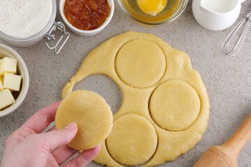 Female hands cutting out a round shape for pastry dough, preparation for the traditional Jewish holiday Purim day. A group of ingredients on the background. top view