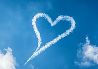 Naklejka premium A heart-shaped trail of smoke drifts across the blue sky from an airplane, symbolizing love and romance in flight. The clean, crisp sky accentuates the unique shape, adding to the dreamy atmosphere.