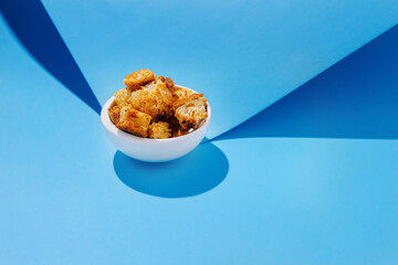 Golden crispy bread cubes in a white bowl against a blue backdrop creating visually appealing contrast