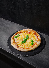 Freshly baked pizza with basil on a dark slate surface in a modern kitchen setting