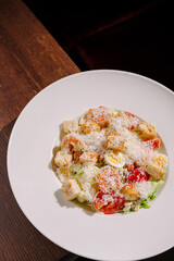 Fresh salad with tomatoes, lettuce, croutons, and cheese served on a white plate at a rustic wooden table