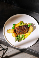 Gourmet dish with grilled steak, potatoes, and asparagus served on a white plate in an elegant setting
