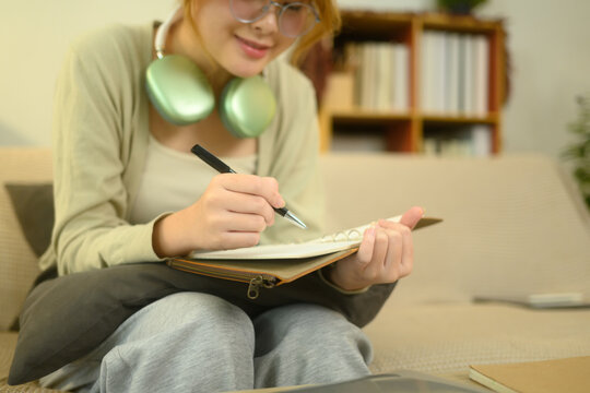 Satisfied young asian woman sitting on couch and writing in a journal