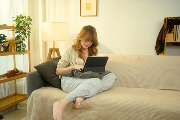 Relaxed young woman using digital tablet for online learning or remote work at home