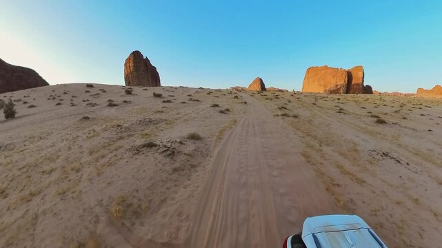 Majestic sandstone mountains glowing orange in the setting sun at Alula Sharaan Nature Reserve, viewed from a car driving through the vast desert landscape of Saudi Arabia. Aerial view
