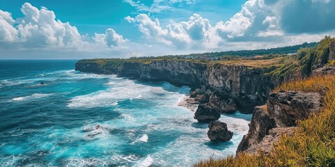 Fototapeta premium Breathtaking coastal vista featuring rocky cliffs and turquoise waves under a clear blue sky with fluffy white clouds in the background.