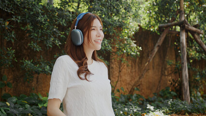 Attractive woman ing headphones enjoys nature in lush garden setting, smiling happily. vibrant...