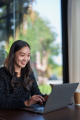 Happy freelancer is working remotely on her laptop in a cafe, enjoying the convenience and flexibility of online work while taking a break