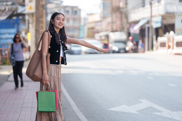 Happy shopper hailing a taxi cab after a successful shopping spree, holding colorful shopping bags and gesturing for a ride on a city street