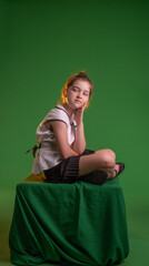 Young schoolgirl sitting thinking and wondering, isolated on chroma key green screen background, workspace mockup. Education advertising concept.