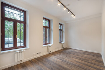 An open space of a room with light walls and dark laminate. Windows with brown frames. Unfurnished.