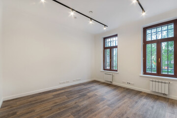 A room decorated in white. Dark laminate floor, windows with brown frames. Unfurnished.