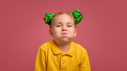 Portrait of preschool girl, child in yellow shirt making funny faces, grimacing against pink studio background. Concept of childhood, emotions, lifestyle, fun, leisure