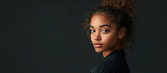Fototapeta premium Portrait of a young woman with a curly hairstyle looking over her shoulder against a dark background with Copy Space.