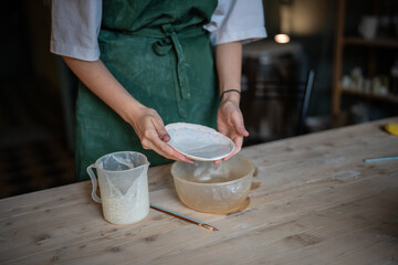 Woman potter hands glaze saucer in workshop for ceramic durability and longevity. Artistic craftsmanship, glazing process, pottery expertise, handmade ceramics, durable finish, DIY, dishes production