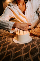 Woman placing candles on a white cake while sitting on the floor in cozy pajamas in a softly lit room