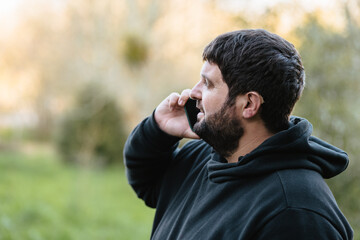 Deaf man using a hearing aid while talking on a mobile phone outdoors in a natural setting