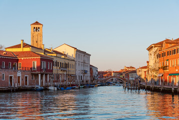 Murano canal with colorful Venetian buildings and arched bridge at golden hour