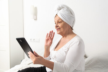 Caucasian senior woman with wrinkles talking with somebody by tablet
