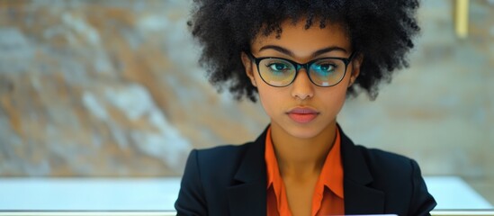 Professional young businesswoman with afro hairstyle and glasses using digital tablet at reception desk in modern office environment