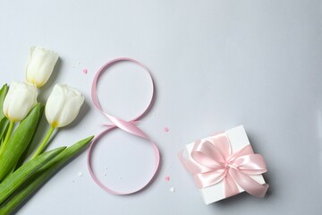 8 March, International Women's Day. Figure eight made of pink ribbon with beautiful tulips and gift box on a gray background. Space for text