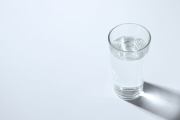 Glass with clear water on white table, space for text