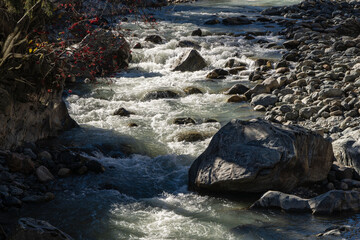 Foamed emerald waters of mountain river breaking through bed among stones and huge boulders. Water...