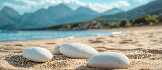 Close up of smooth white pebbles on sandy beach with tranquil mountains in background and ample space for text or overlay designs