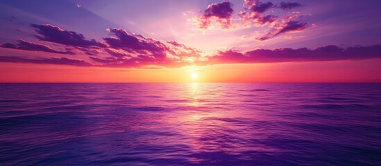 Obraz premium Vibrant sunset sky with purple pink and orange hues reflecting over the tranquil sea creating a serene background with ample space for text.