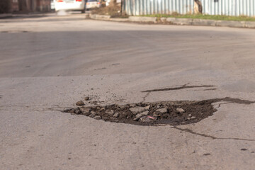 Pothole in the road with a car moving away in the background