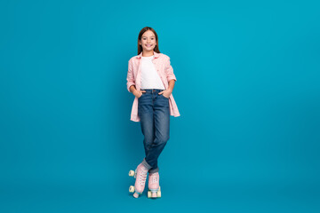 Young girl wearing trendy casual outfit posing with roller skates on blue studio background