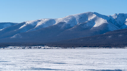 Snowy Peaks Overlooking Khovsgol - The majestic snowy peaks surrounding the frozen Khovsgol lake stand tall against a bright blue sky, offering a pristine winter view.